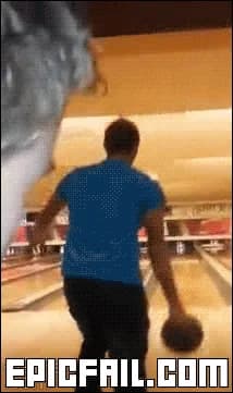A man at a bowling alley winds up and throws, and the ball flies back toward the camera.